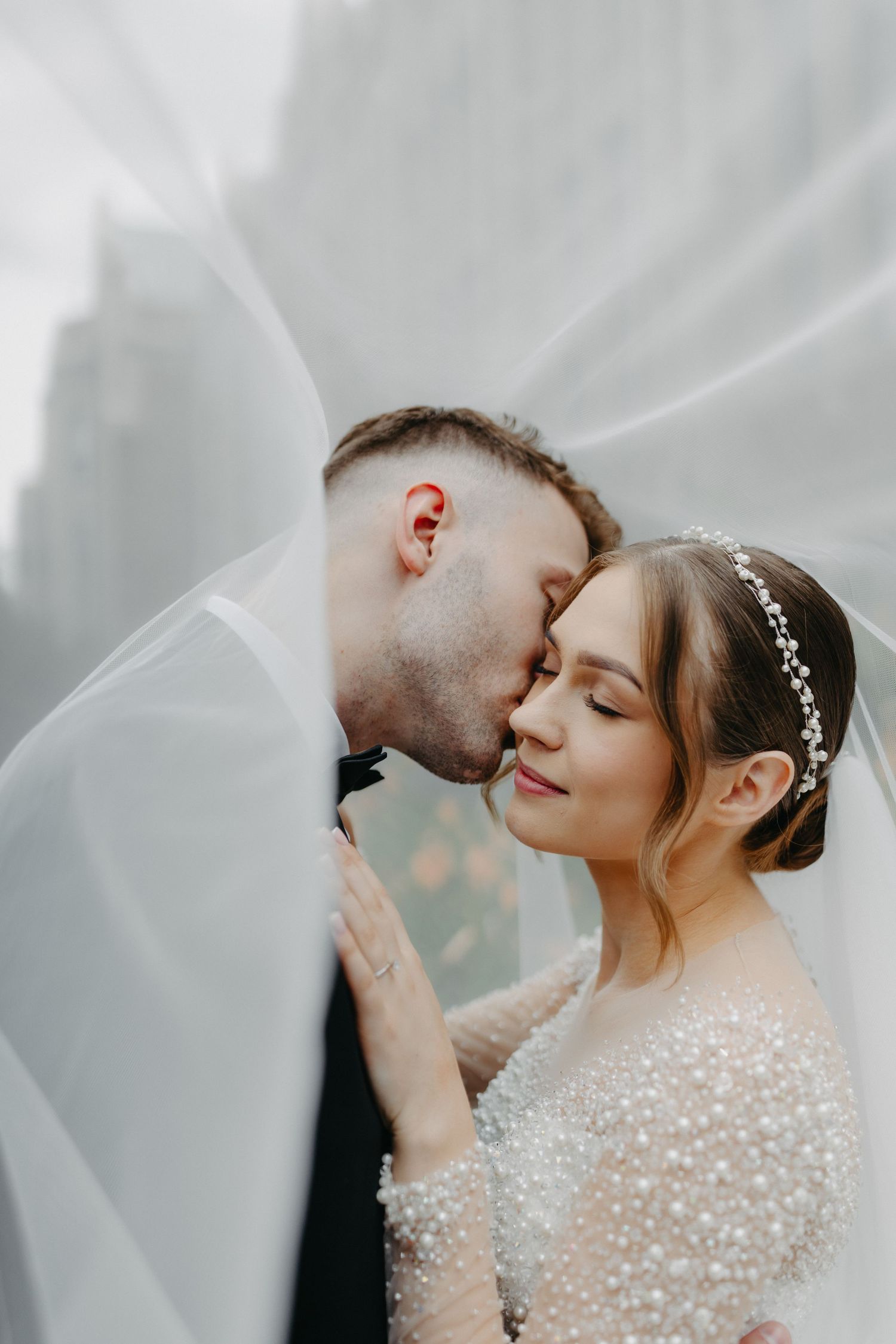 Romantic wedding portrait under flowing veil with intimate moment.
