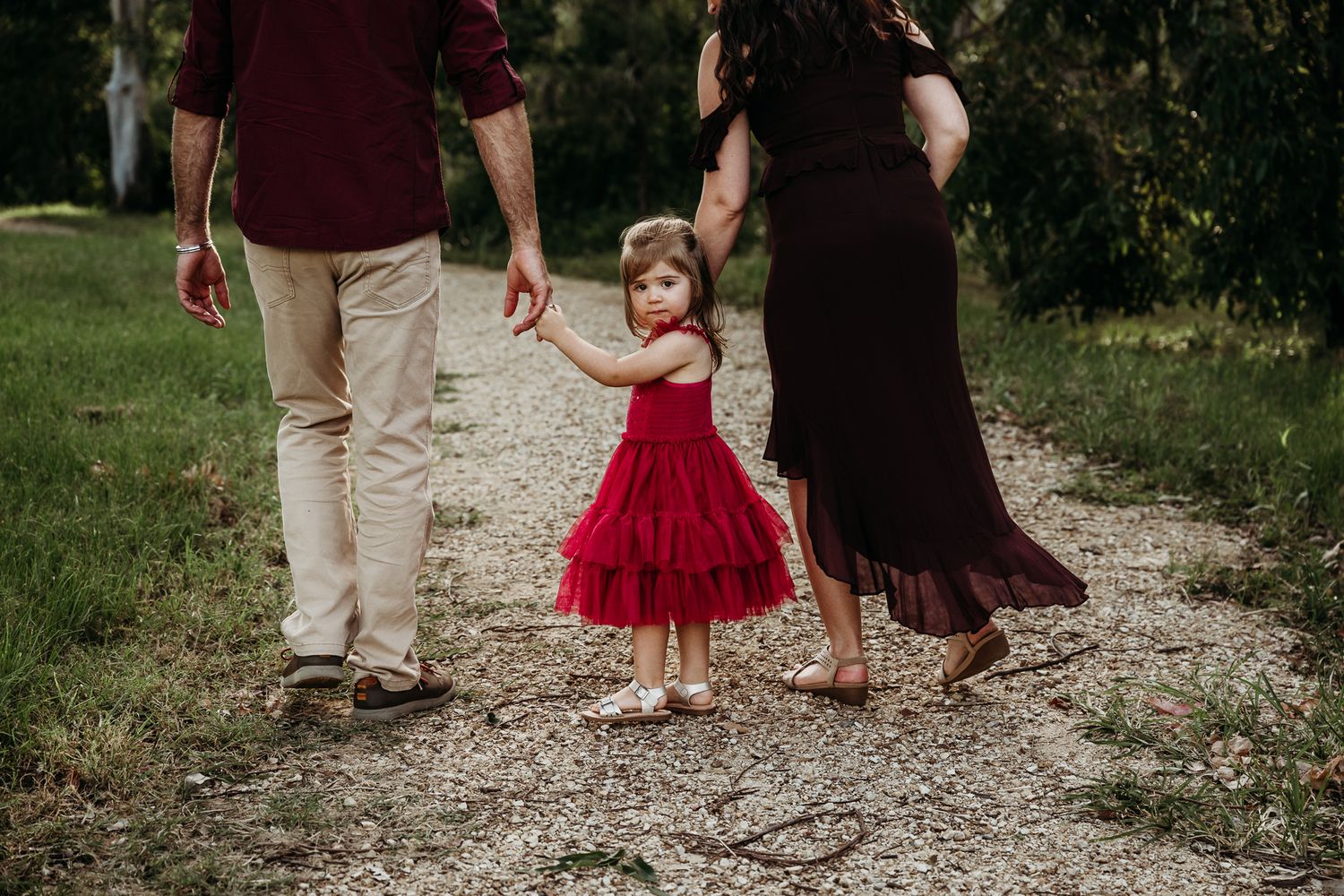 Little girl in red dress walks path with adults in countryside setting.