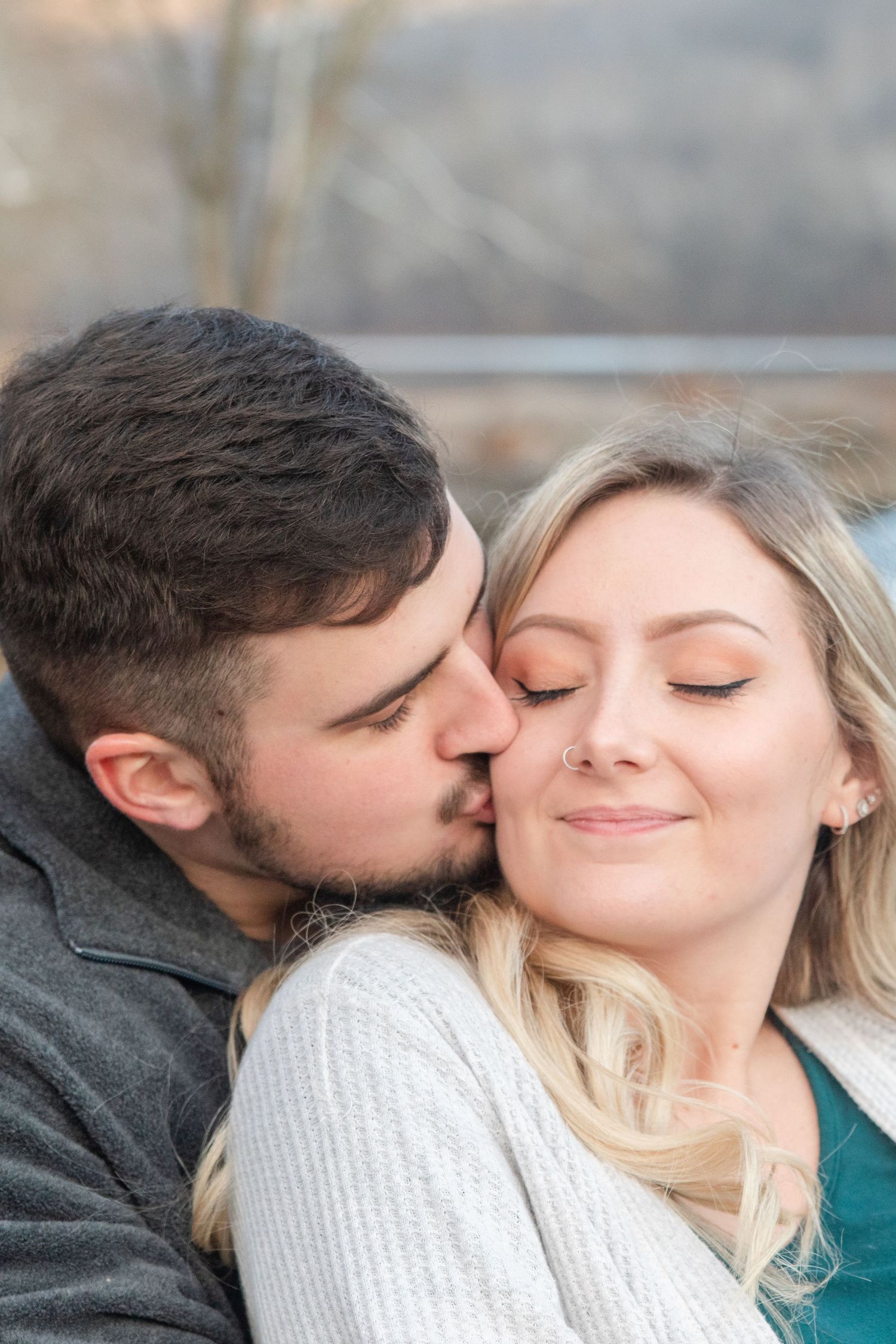 A romantic moment captured outdoors with a couple in white and grey sweaters sharing an intimate embrace.