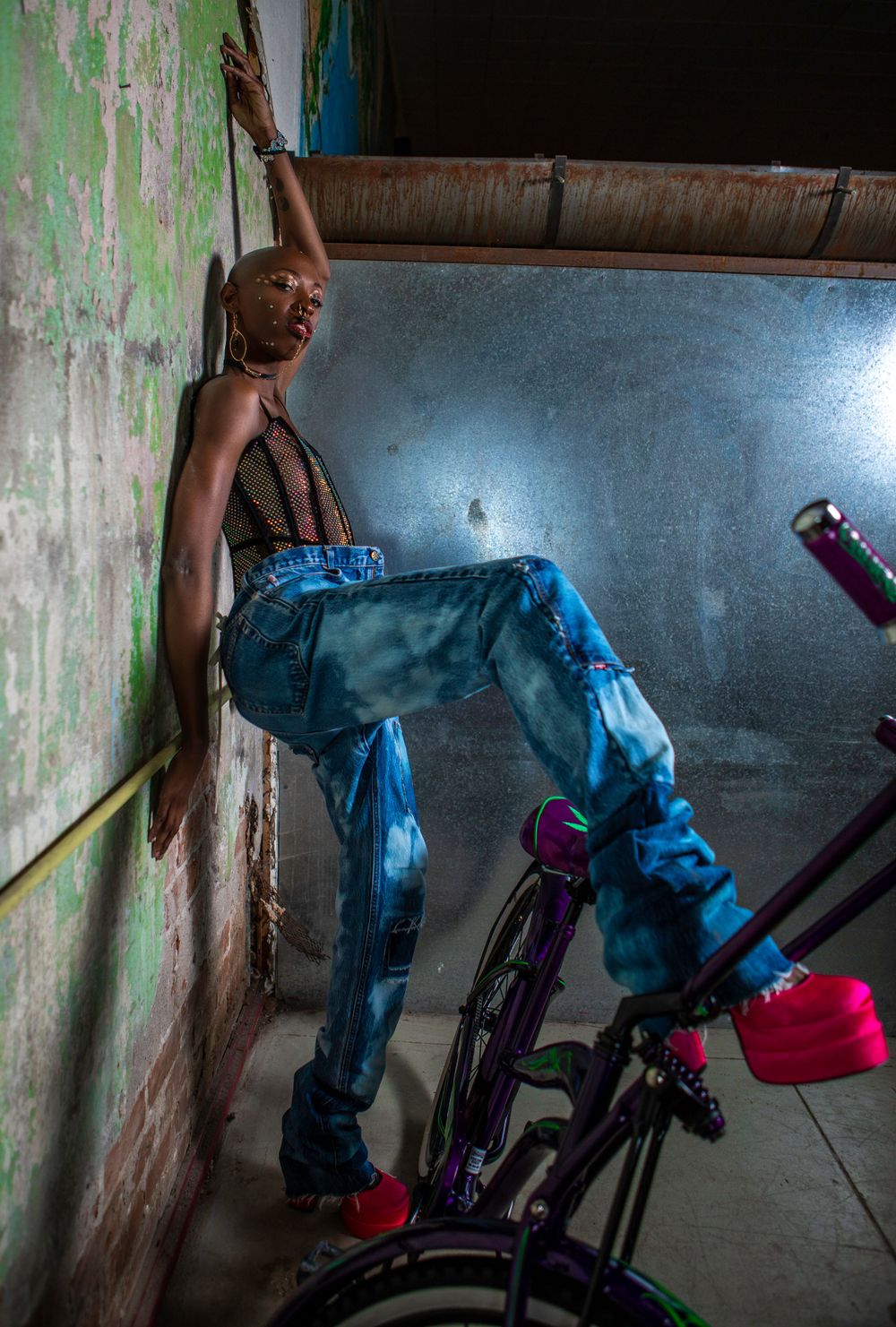 Urban fashion shoot with model in denim against grungy wall with bicycle.