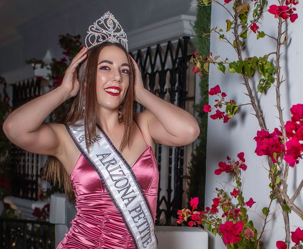 Beauty pageant contestant in pink gown and crown poses with flowers.