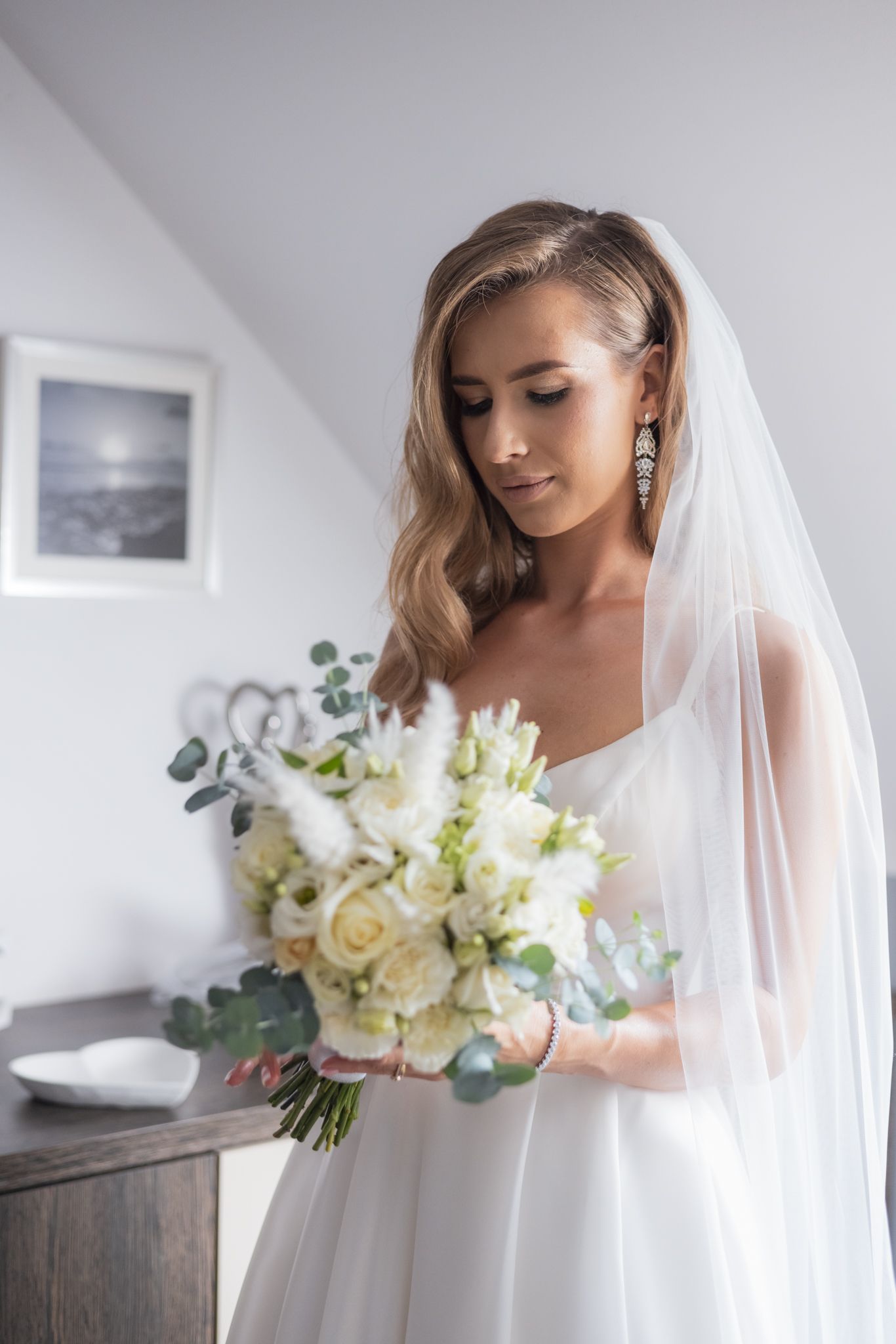 Elegant bride in white dress holding a bouquet of white roses and eucalyptus.