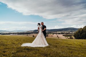 Wedding couple standing in field with mountains and cloudy sky background.
