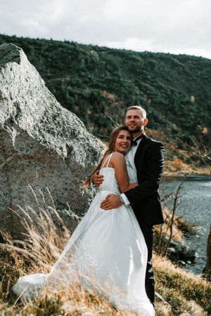 Wedding couple posing by white cliffs with water and mountains in background.