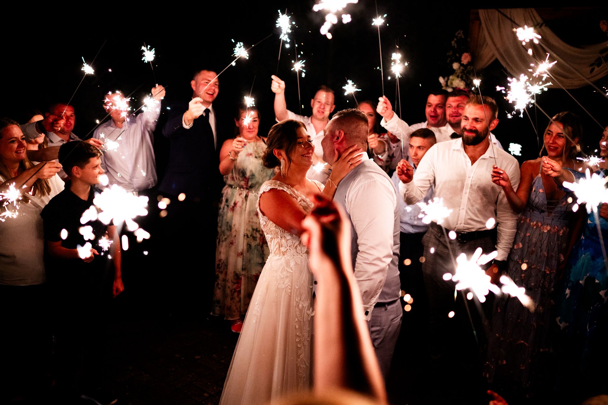 Wedding celebration at night with sparklers creating magical light effects among dancing guests.