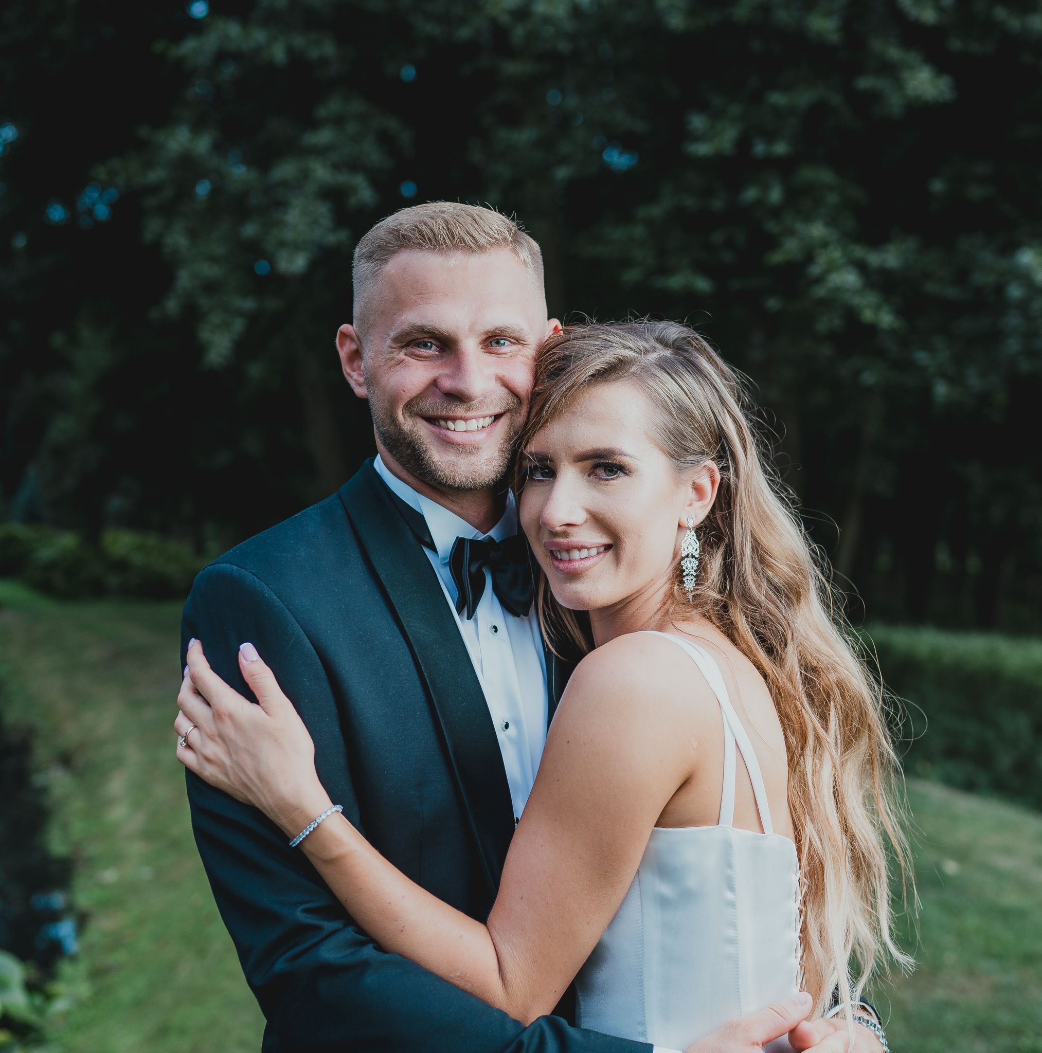 Elegant couple in formal attire share intimate embrace during outdoor wedding photoshoot.