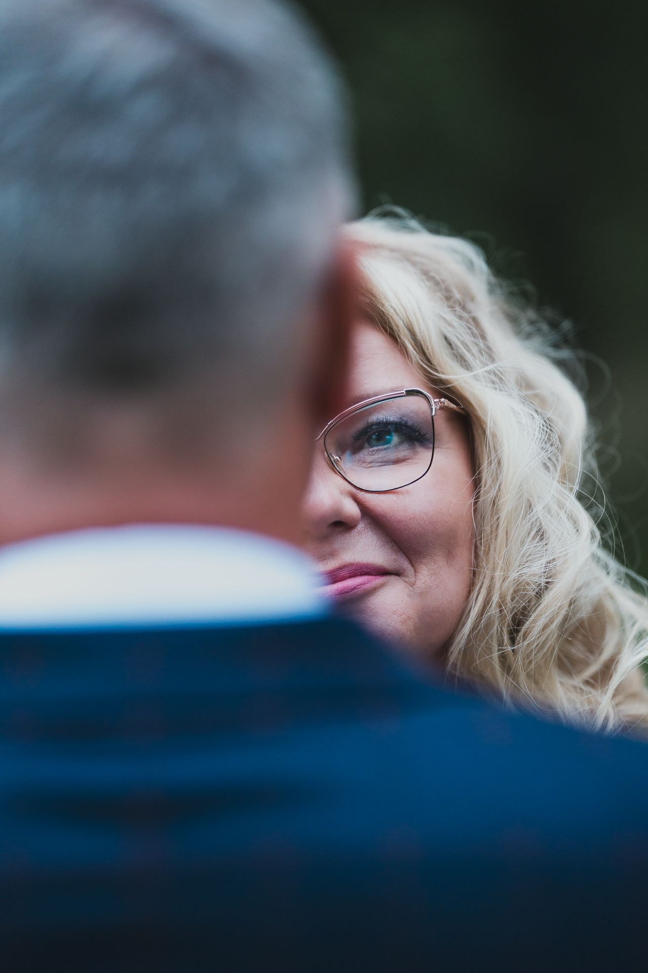 Close up romantic wedding portrait showing glasses and blonde curls against natural background.