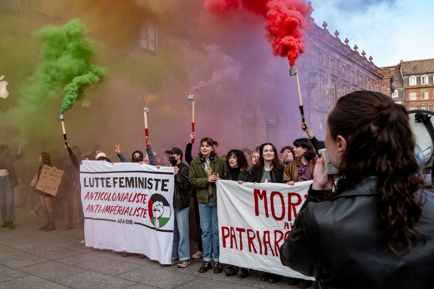 Protesters with colorful smoke flares holding banners during a feminist demonstration.