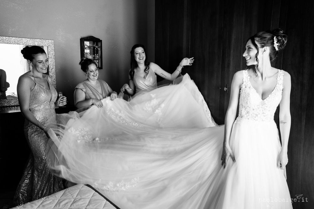Bridesmaids help arrange flowing wedding dress train in black and white photography.
