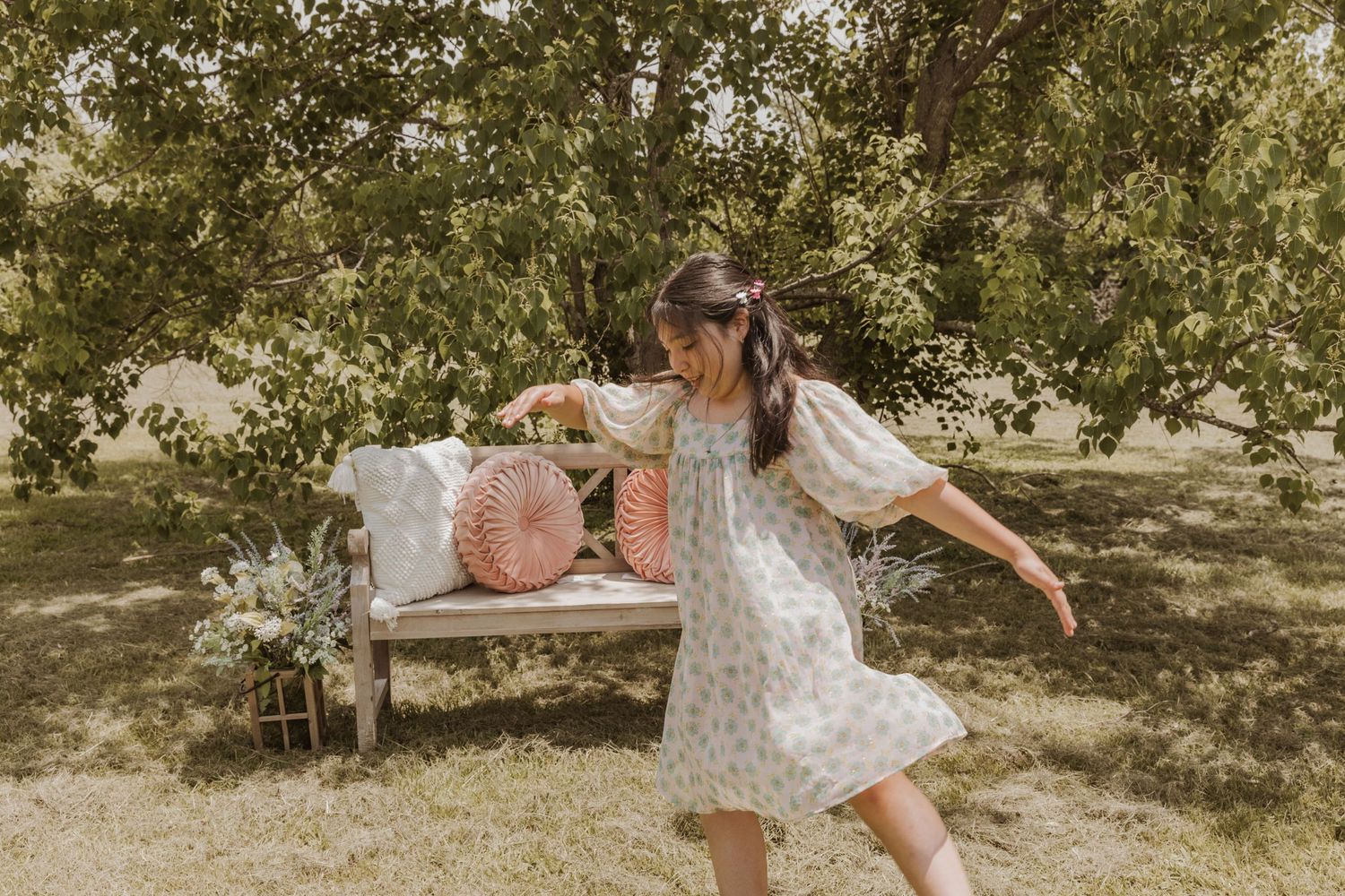 Vintage-inspired garden scene with floral decorations and a white bench in dappled sunlight.