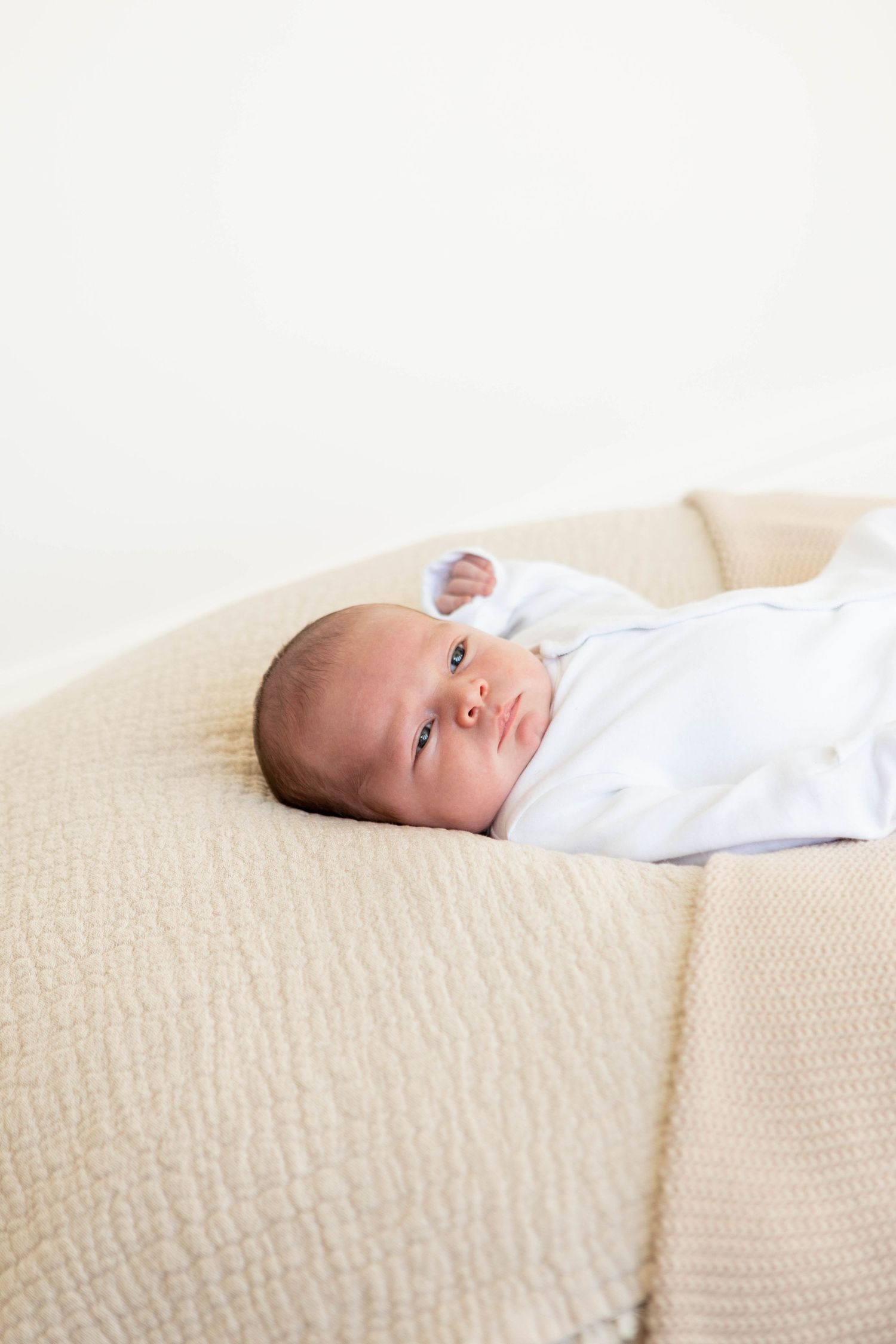 newborn baby showing his eyes laying on posing bag during newborn photography session