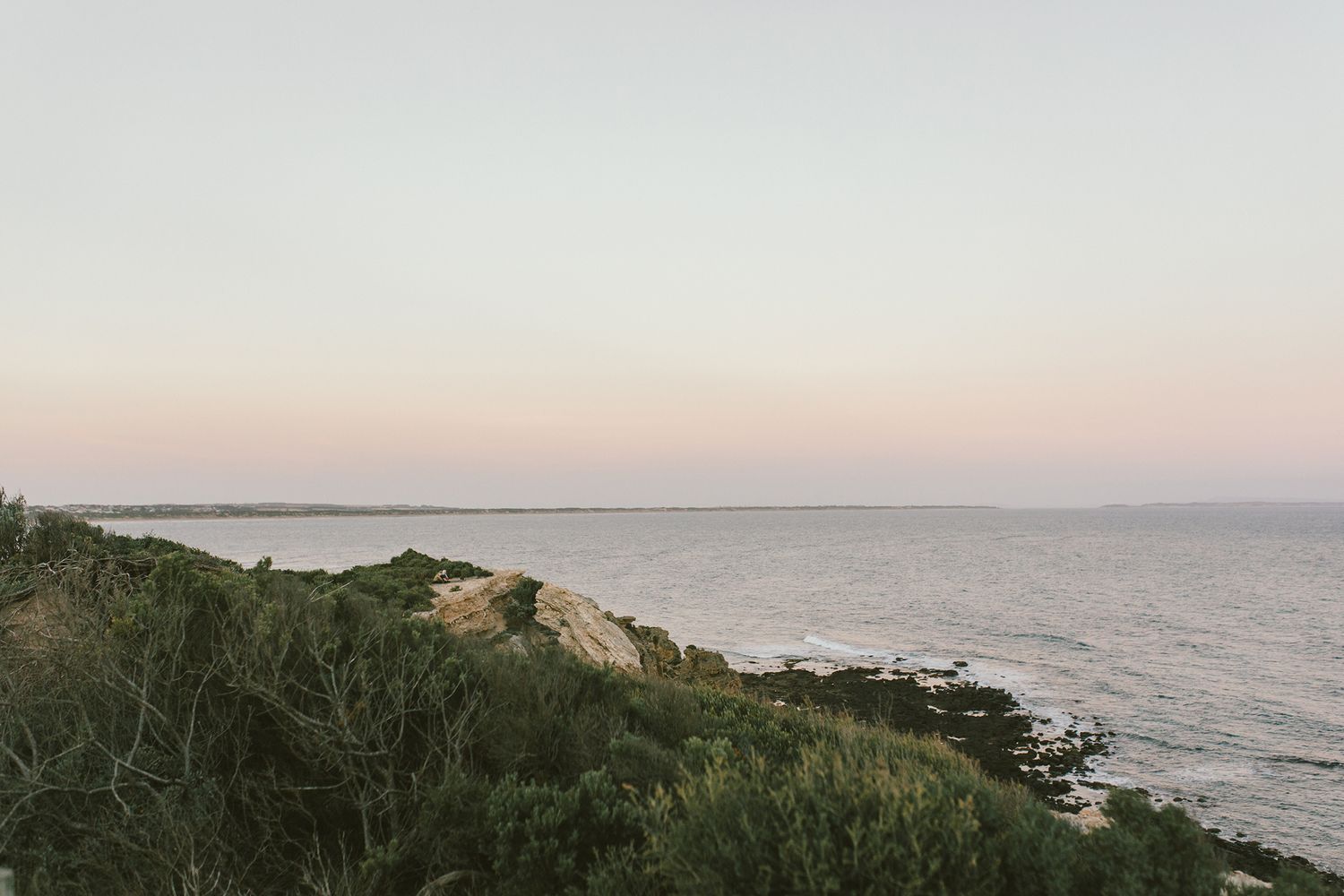 Scenic coastal landscape at dusk showing cliffs and ocean under pastel sky.