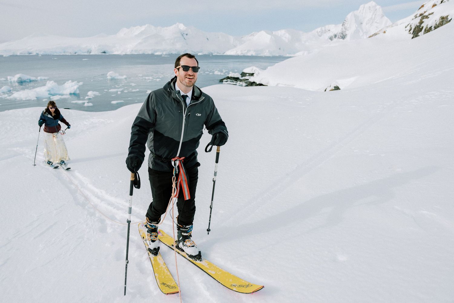 Person skiing on snowy slope with Antarctic mountains and ocean in background.