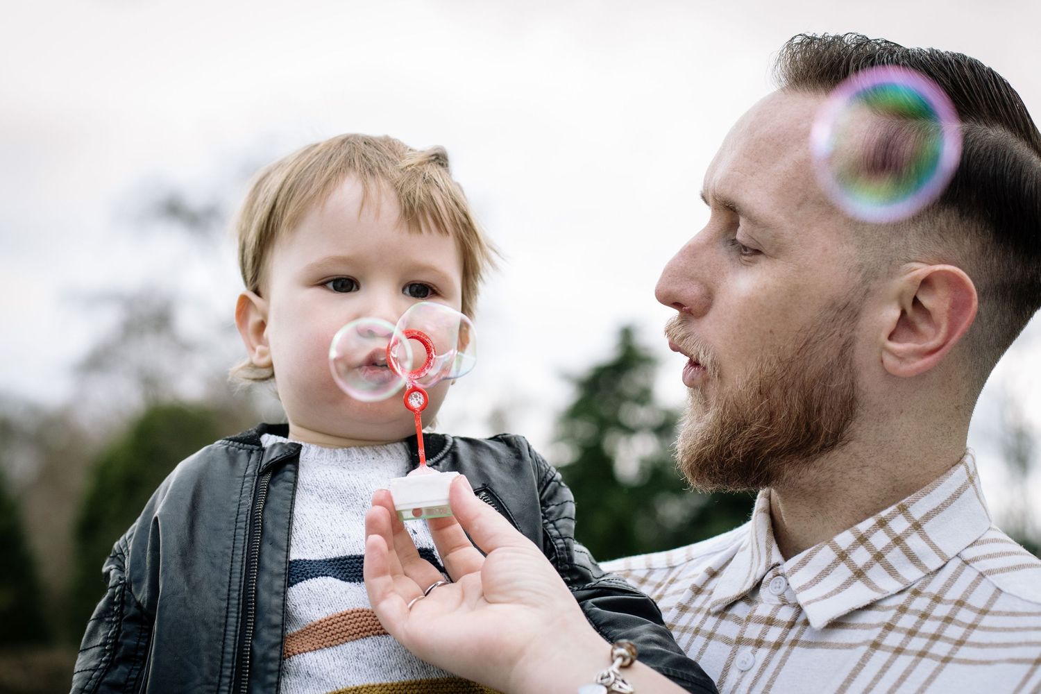 A tender moment of blowing bubbles together outdoors on a cloudy day.