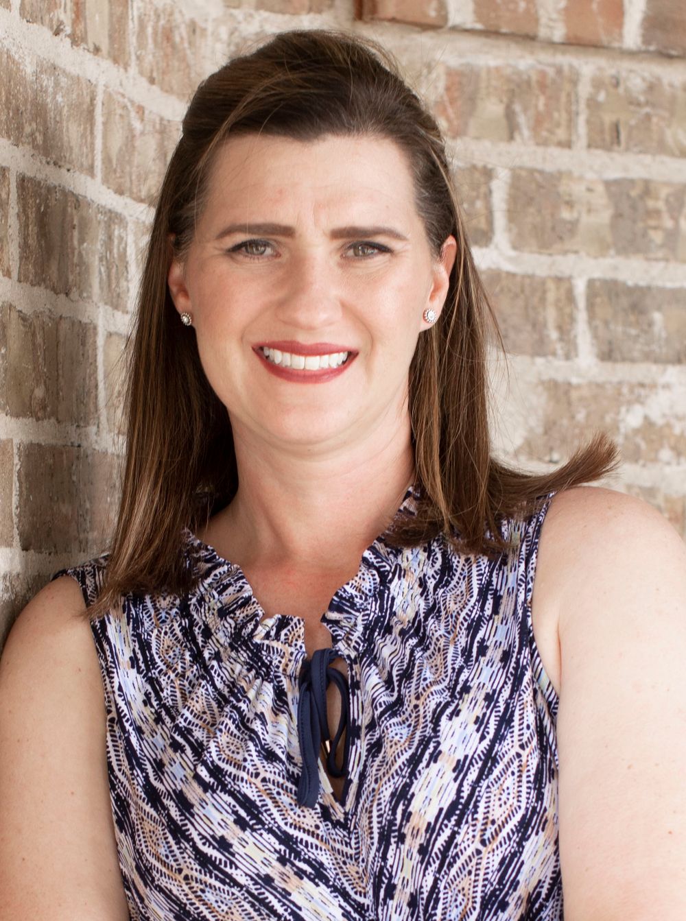 Professional headshot of woman in patterned sleeveless top against brick wall.