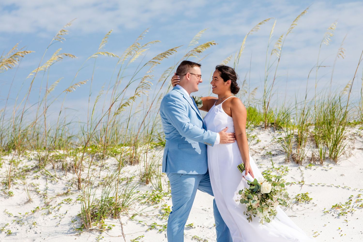 A couple shares an intimate moment among beach grass and sand dunes on their wedding day.
