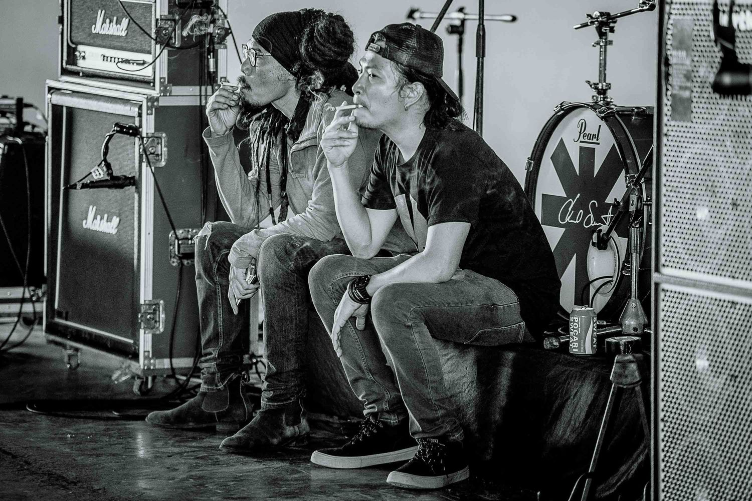 Musicians take a break backstage next to large amplifier stacks.