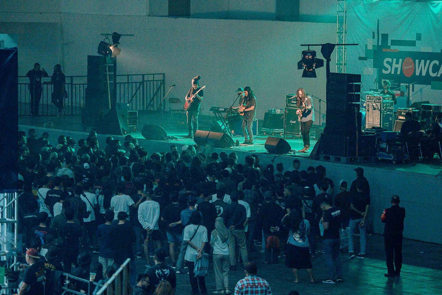 Crowd watching band perform on stage with teal lighting at an indoor venue.
