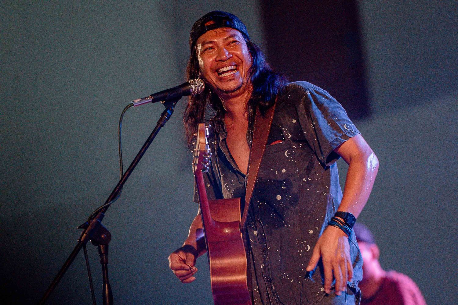 Performer singing with acoustic guitar under stage lighting.