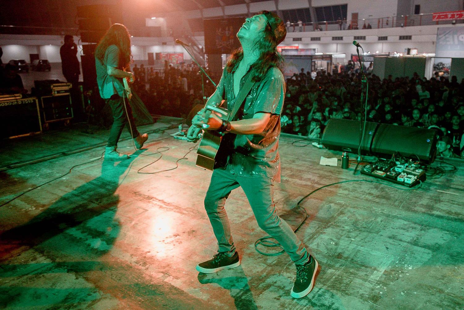 Guitar player performs under green stage lighting at indoor venue.