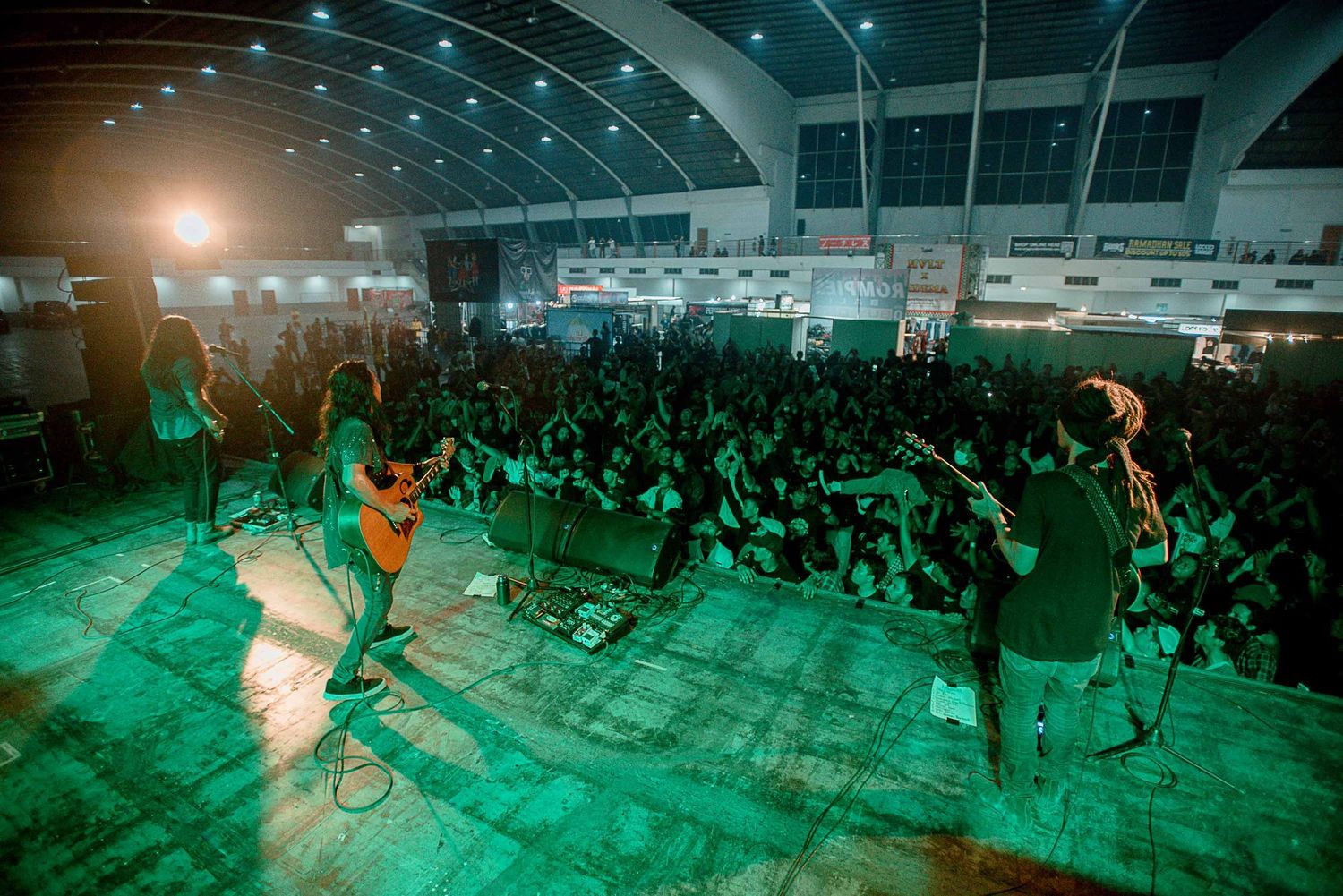 Wide shot of band performing on stage with green lighting and large crowd.