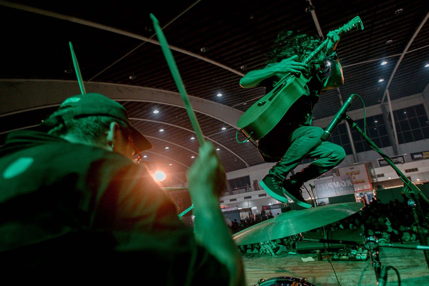 Musicians performing under green stage lighting with dramatic motion blur effects.