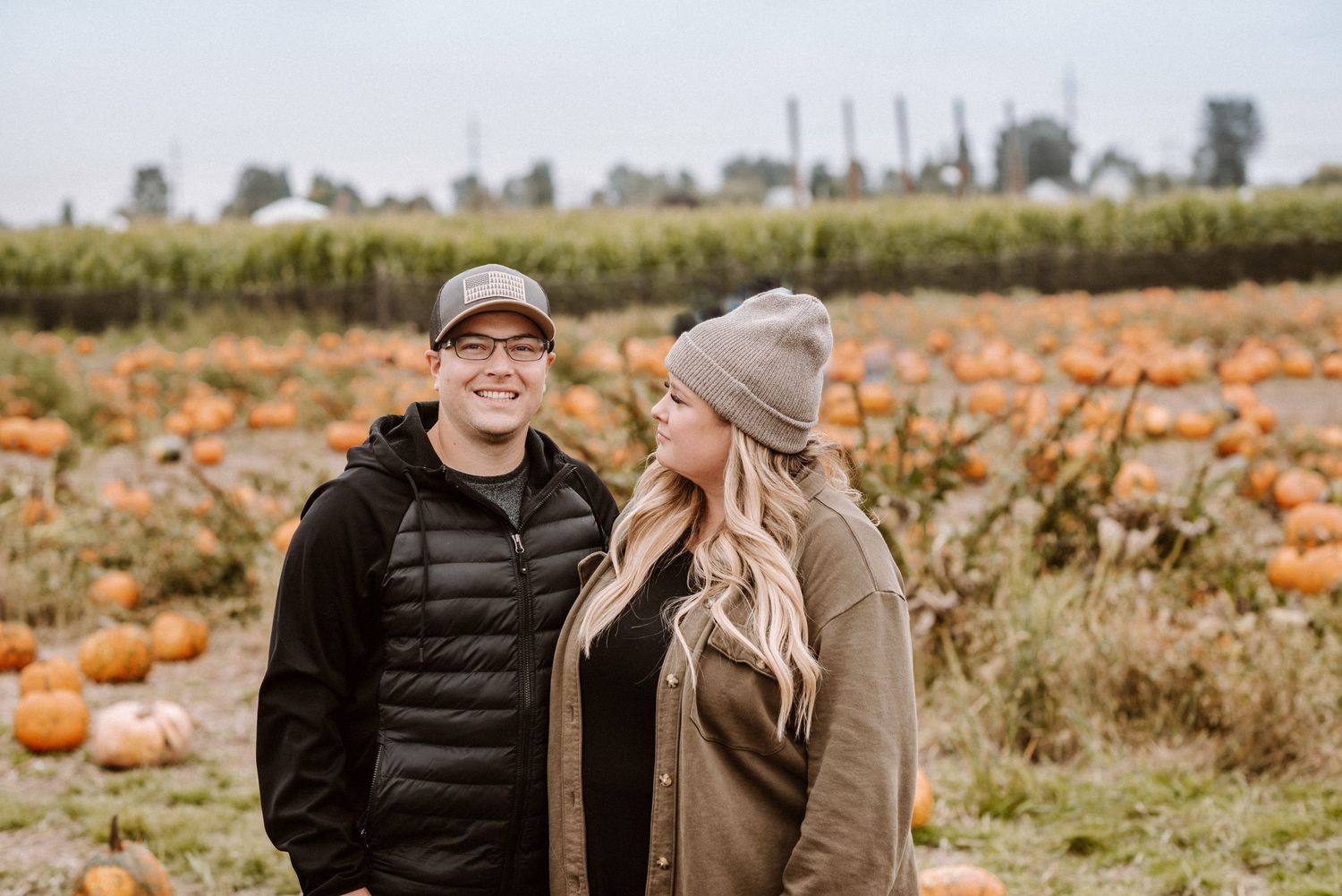 A couple enjoying autumn at a pumpkin patch wearing warm clothing.