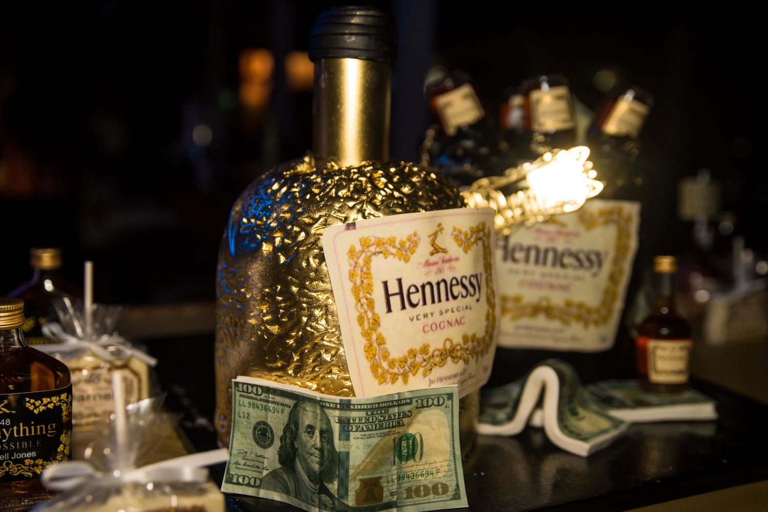 Collection of liquor bottles with Hennessy and decorative lighting in a dark setting.