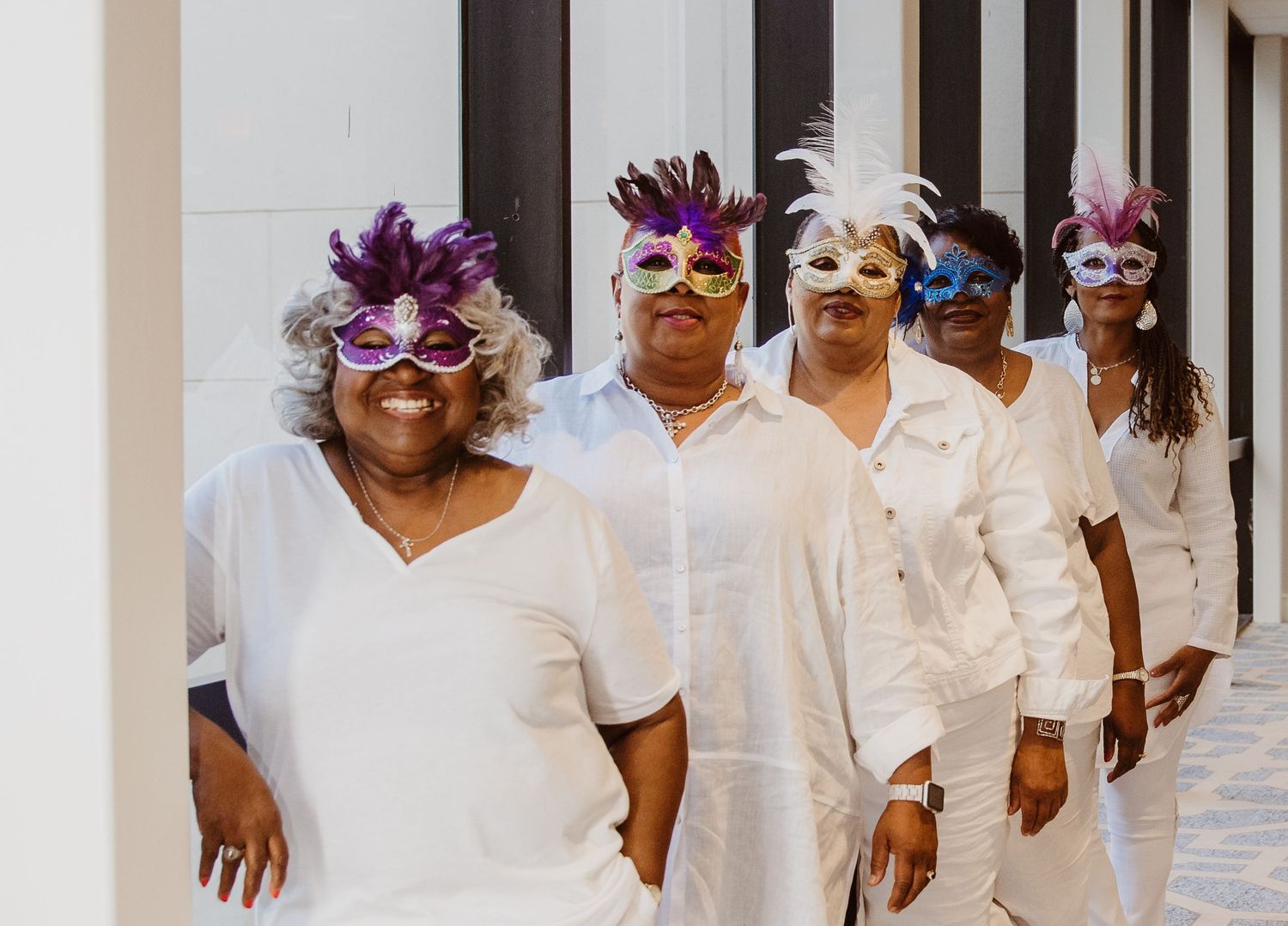 Group wearing all-white outfits walking down a hallway with decorative masquerade masks.