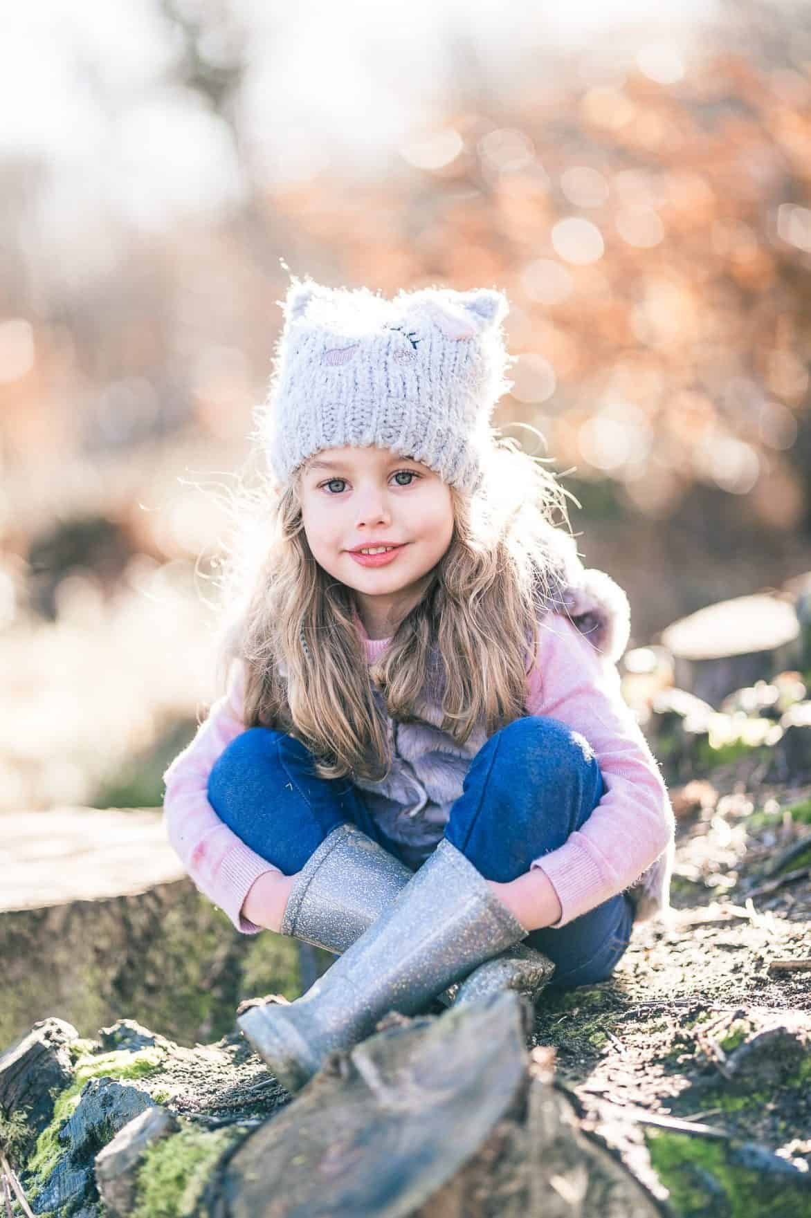 Child wearing cute knit cat ear beanie sitting outdoors in winter.