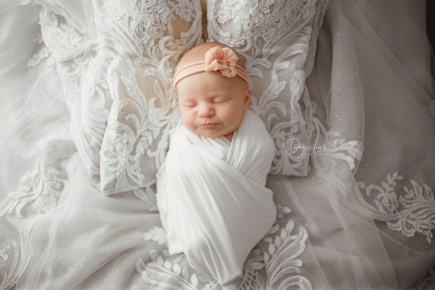 Newborn baby wrapped in white fabric lying on delicate lace textiles.