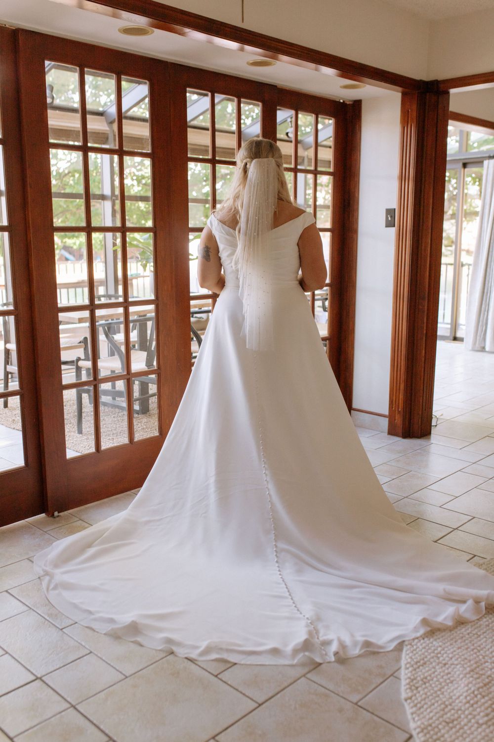 Elegant white wedding dress with long train shown from behind in a bright interior space.
