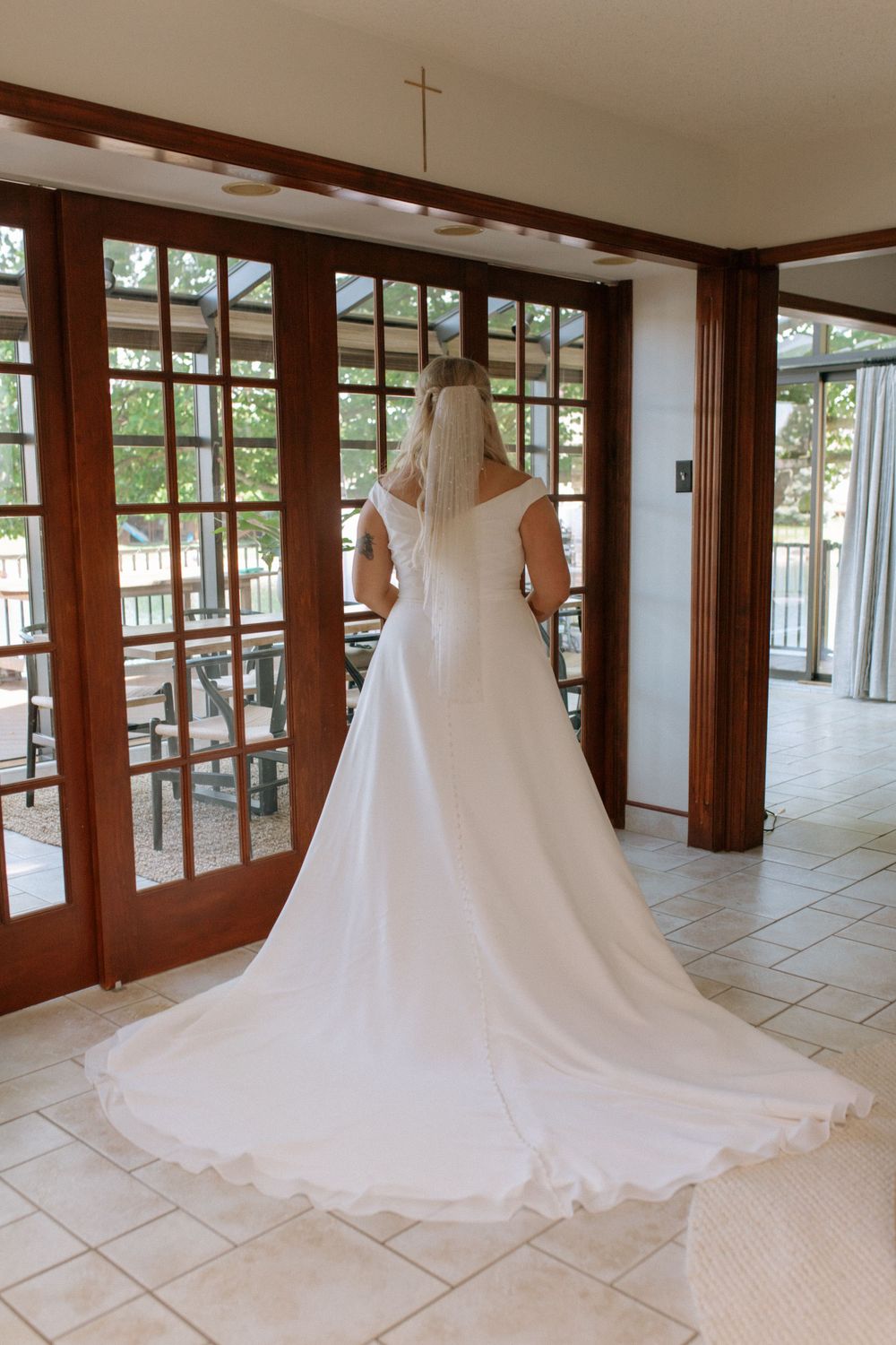 Back view of white wedding dress with cathedral train in a sunlit room with French doors.