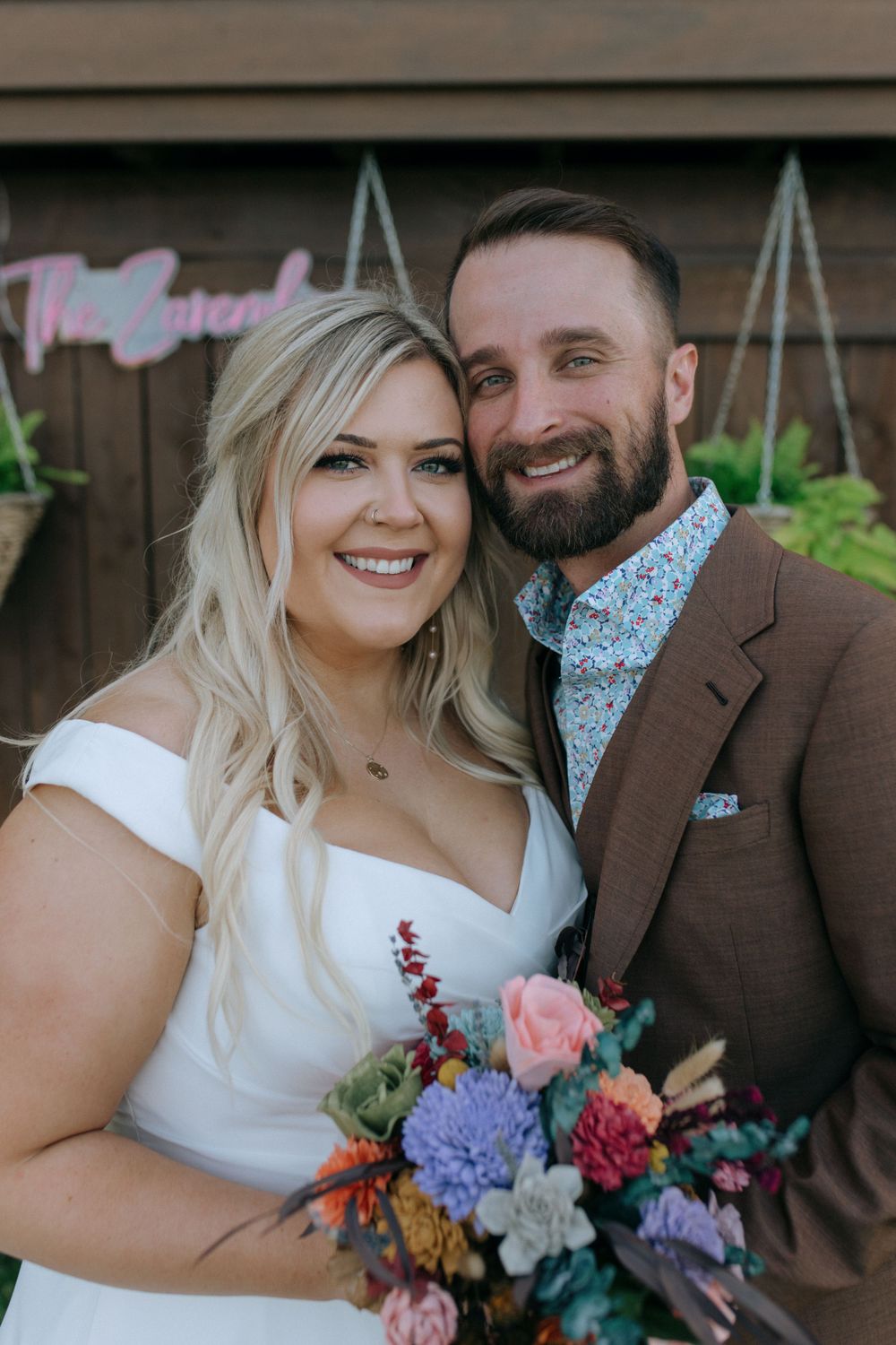 A joyful wedding portrait featuring a couple with the bride holding a multicolored bouquet.