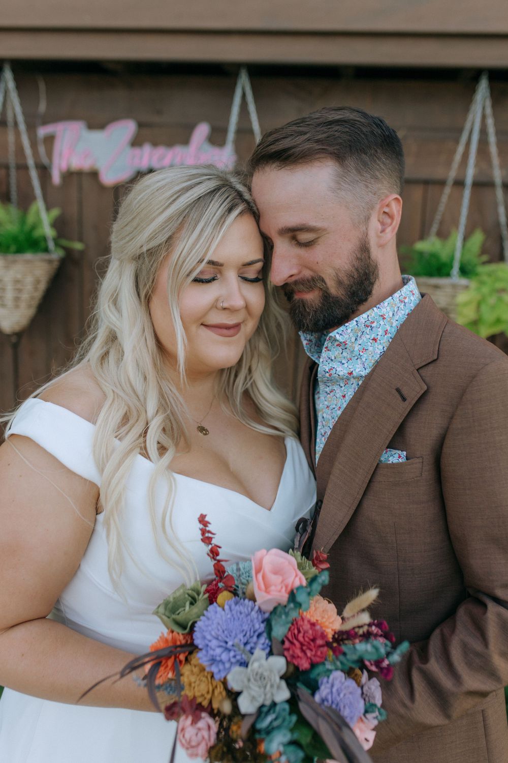 Intimate portrait of newlyweds with colorful bouquet against brown wall backdrop.