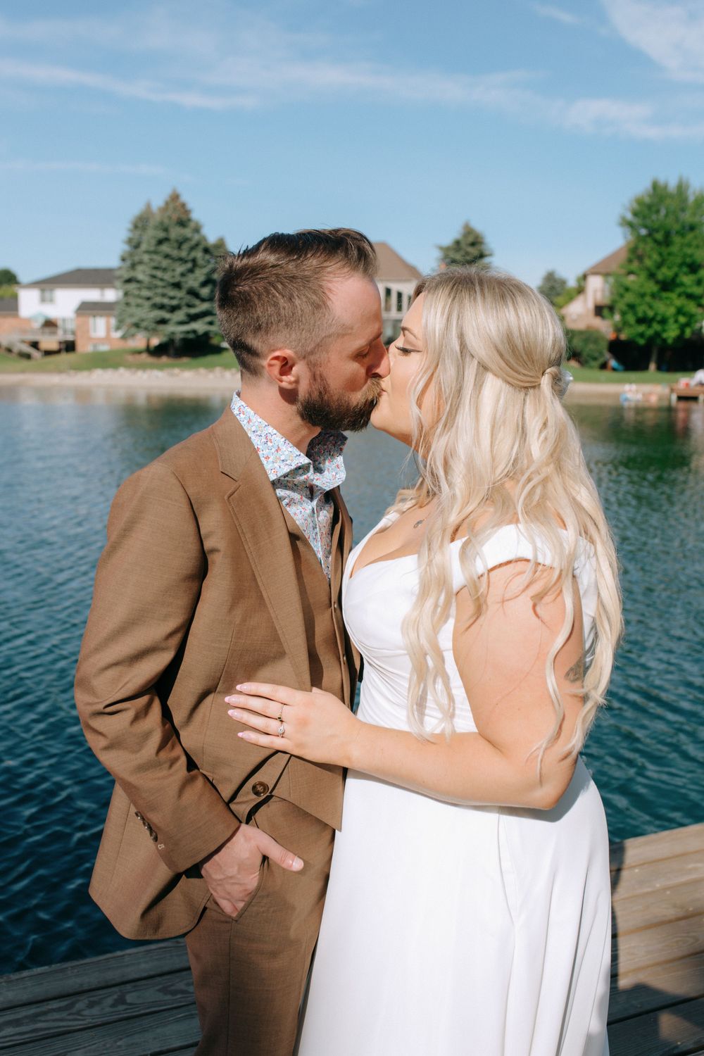 Romantic lakeside wedding portrait with couple kissing on wooden dock.