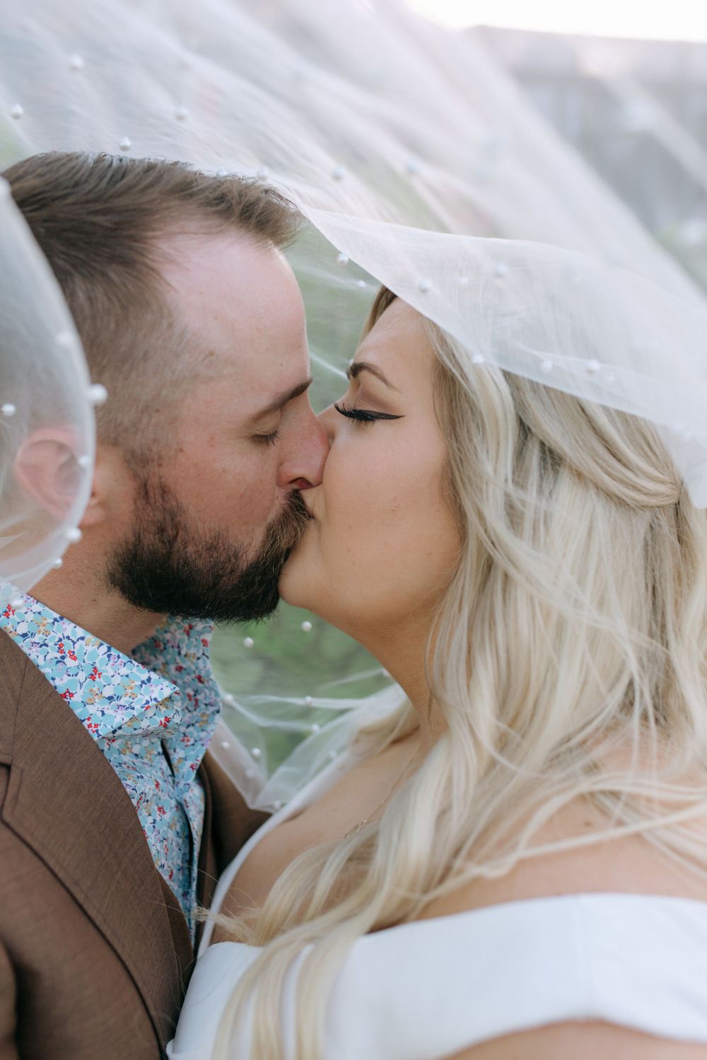 Romantic kiss beneath wedding veil with soft lighting.