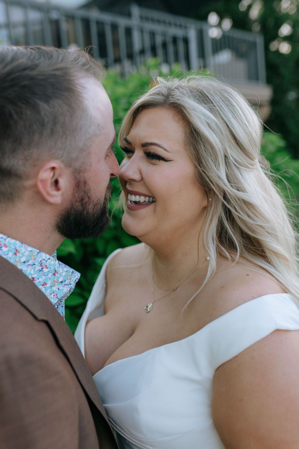 Joyful couple in brown suit and white dress sharing an intimate moment outdoors.