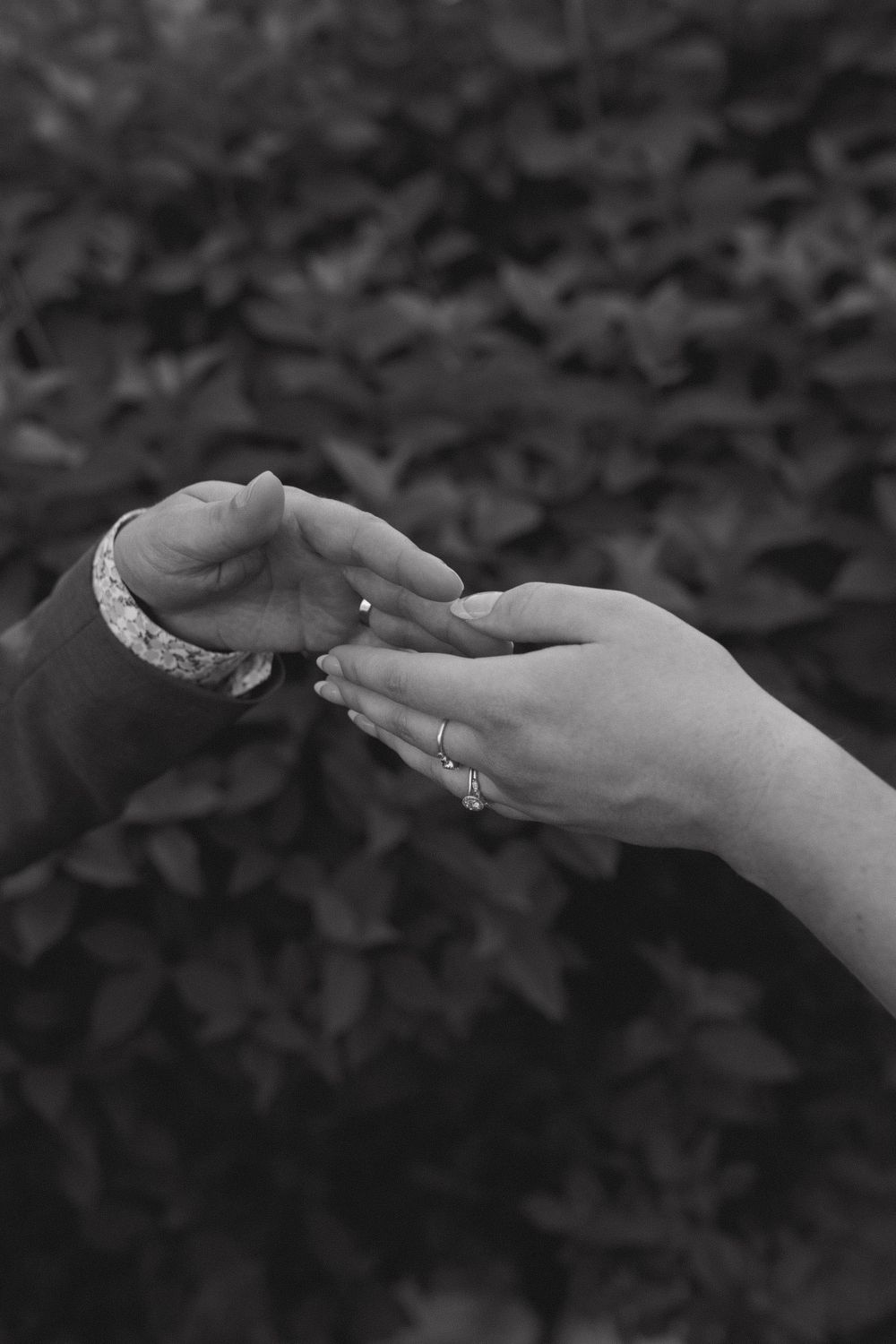 Black and white photo of hands touching with engagement ring visible.