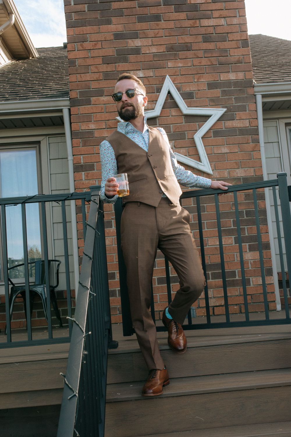 Person in brown vest and suit stands confidently on porch against brick wall with decorative star.