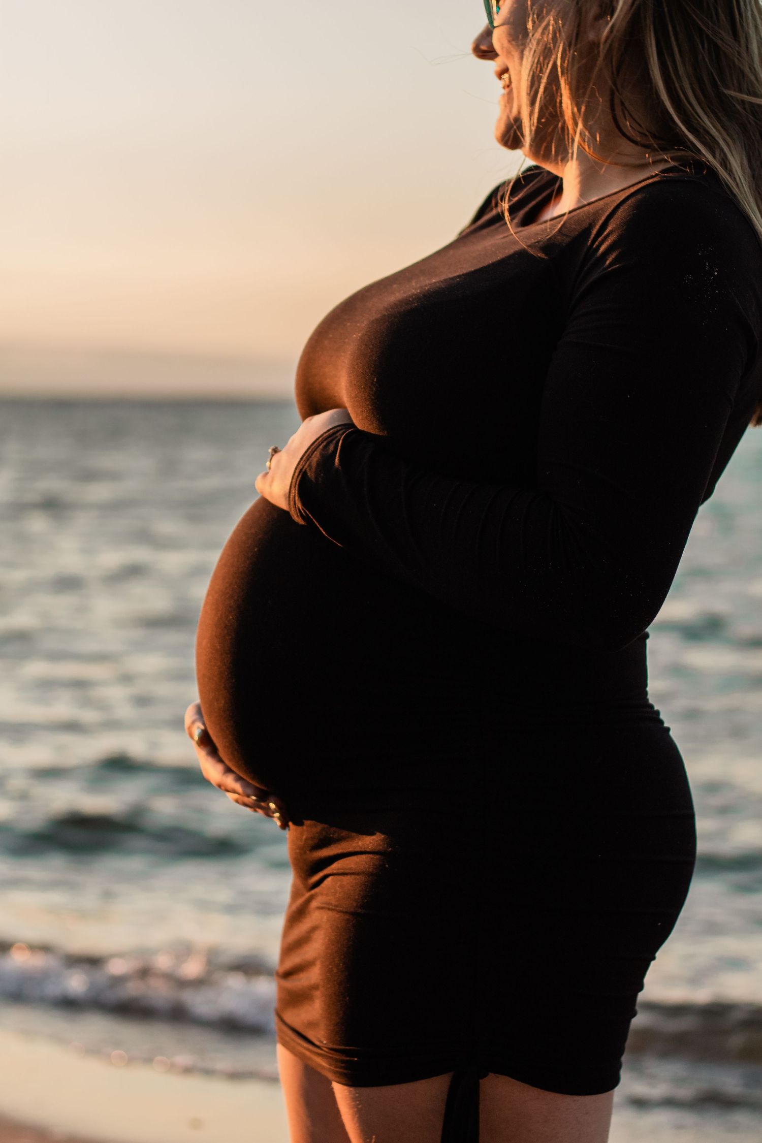 Silhouette of pregnant woman's belly against sunset ocean backdrop.