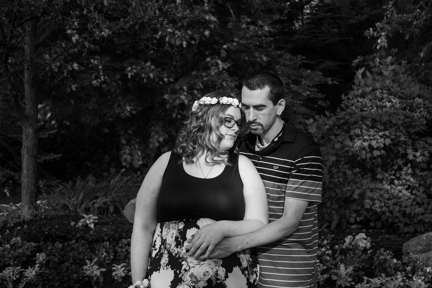 A black and white intimate portrait of a couple embracing in a garden setting.