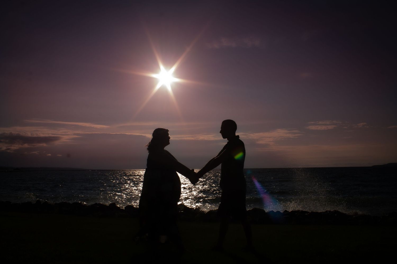 Two silhouettes holding hands against a dramatic sunset over the ocean.
