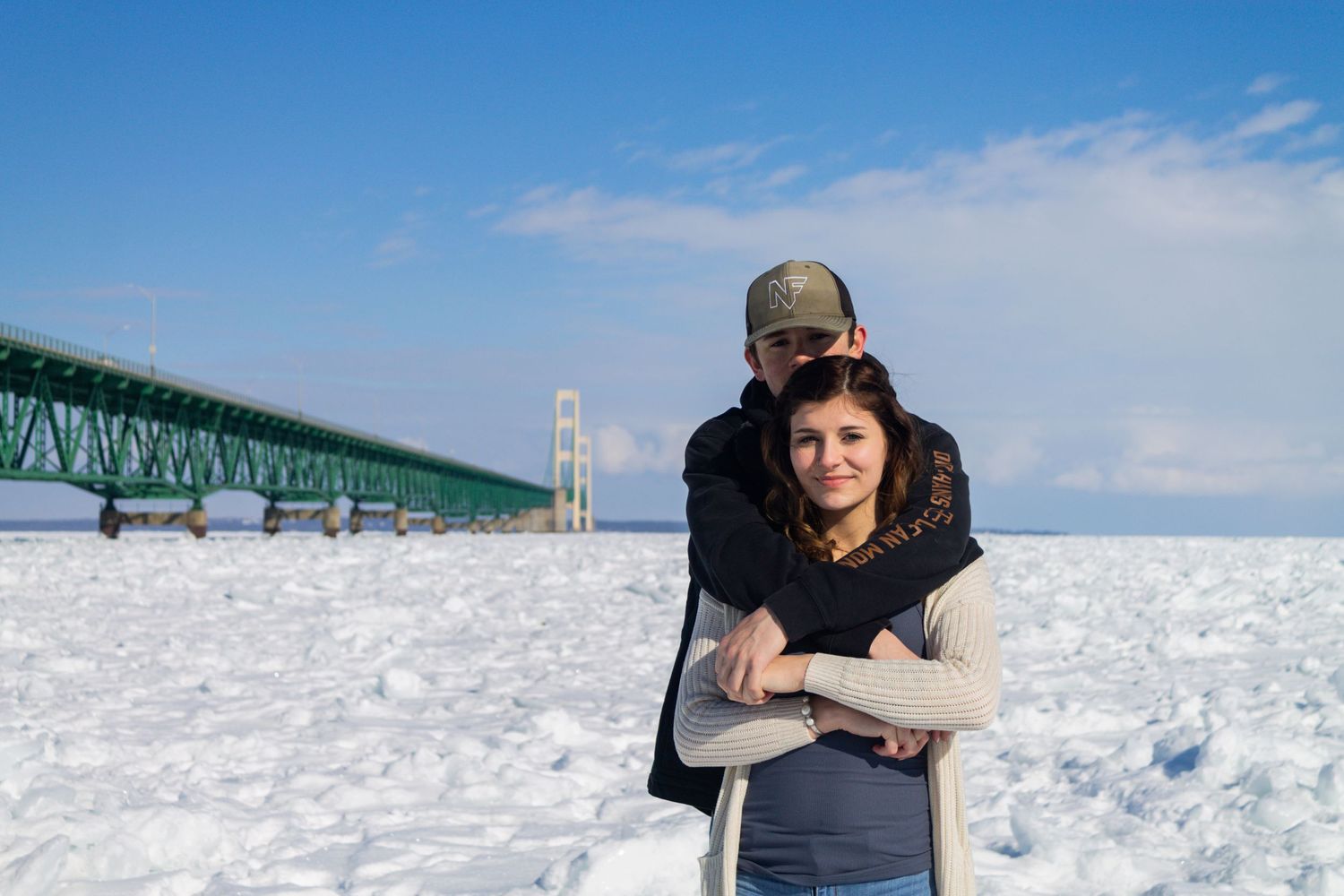 Couple embraces in front of the Mackinac Bridge on a snowy winter day in Michigan.