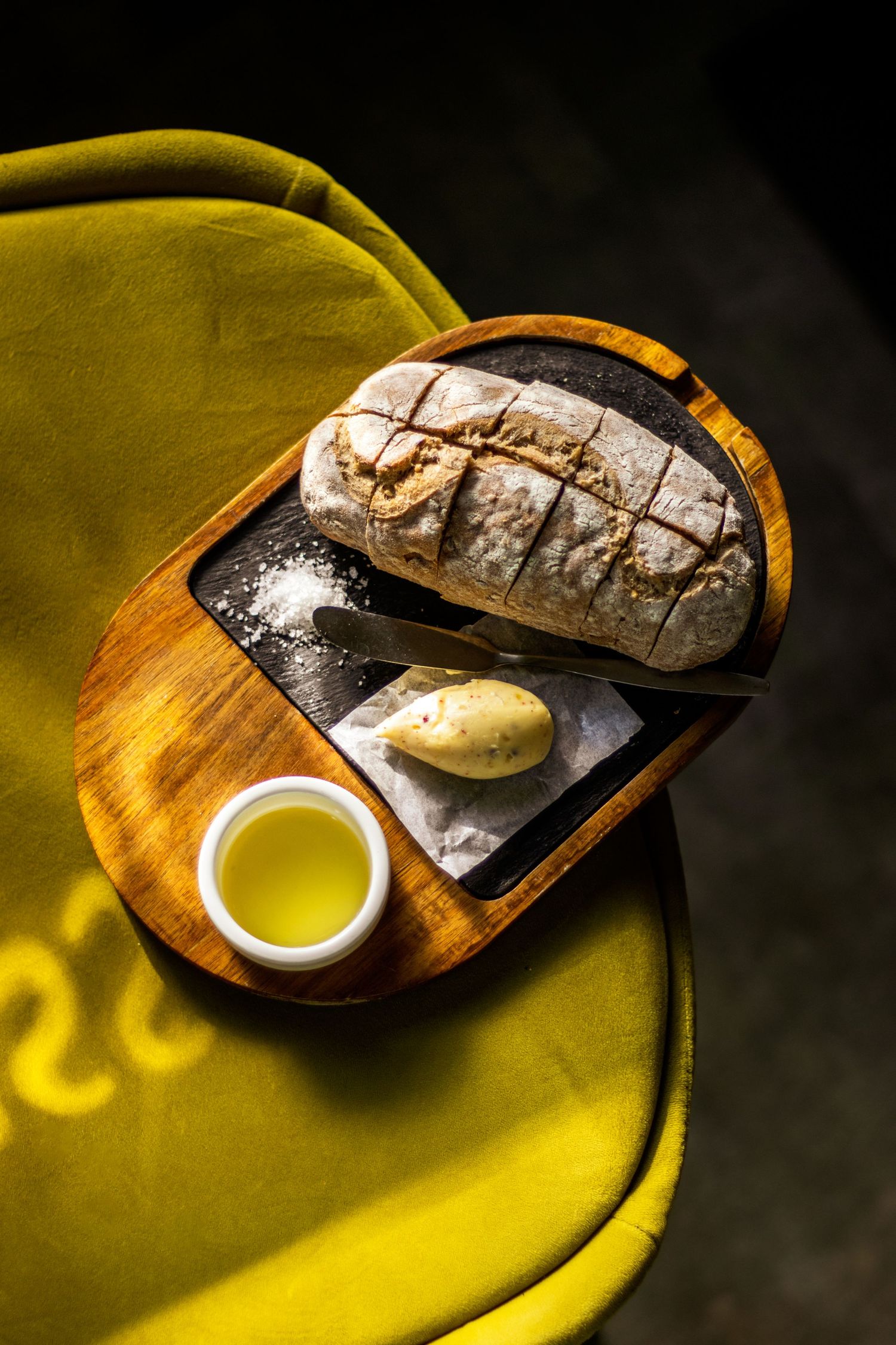 Stilleven van brood en boter op groene fluweel, gevangen in zonlicht.