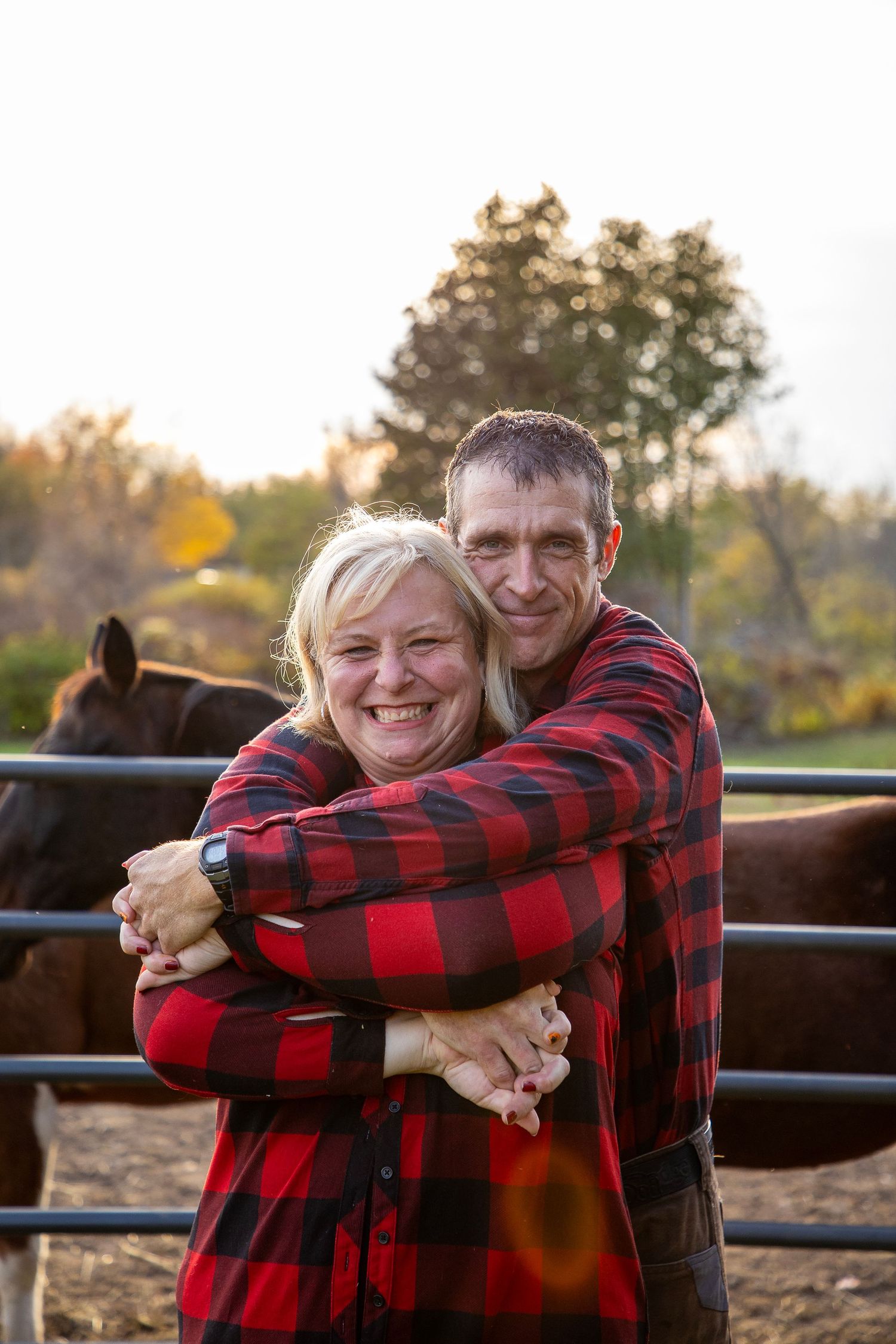 A couple with the man behind bear hugging his wife with horses behind them