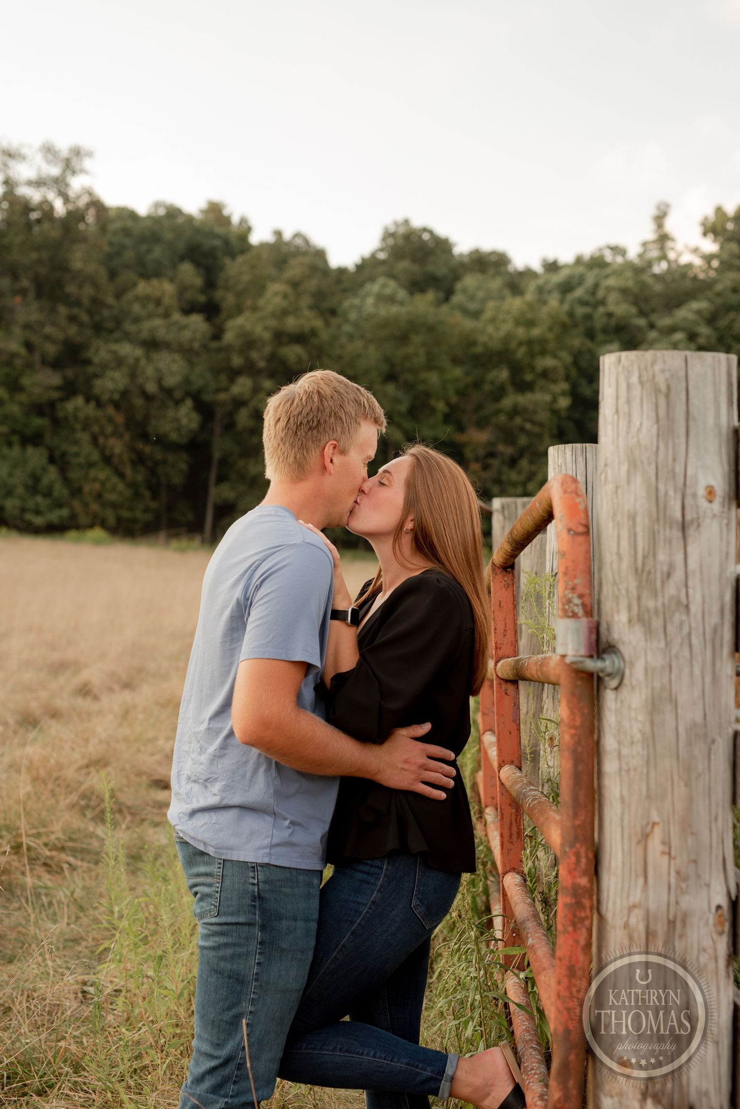 Intimate moment shared between couple by rustic wooden fence post in golden light.
