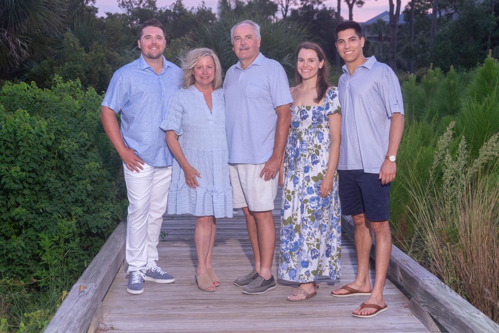 Family of five posing together on wooden boardwalk surrounded by lush green foliage.