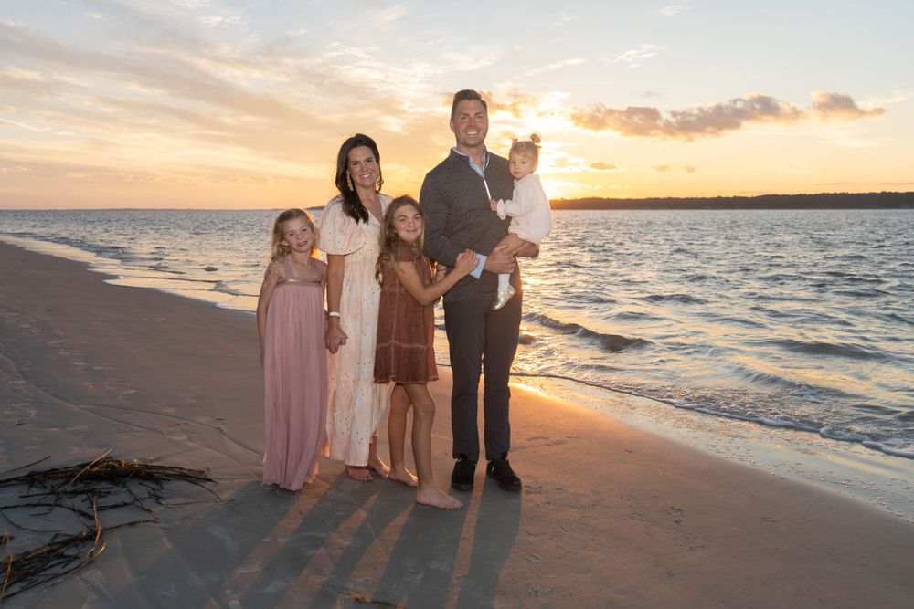 Family of five posing on Sea Pines Tower Beach at golden sunset, parents with three young children smiling by the ocean.
