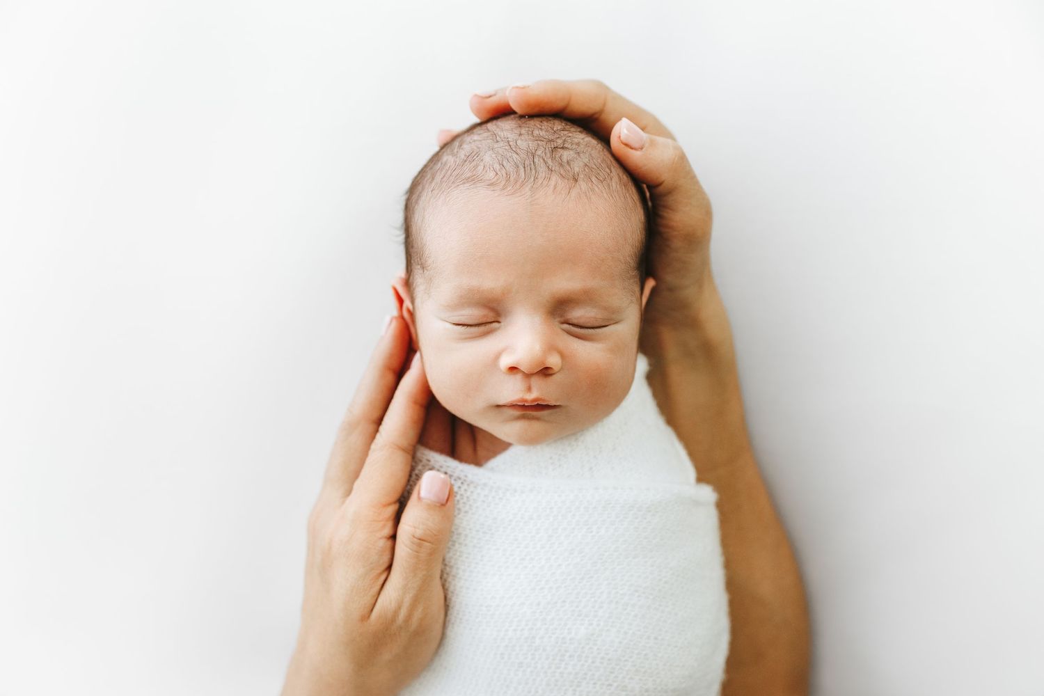 Newborn Boy swaddled, head in parents hands